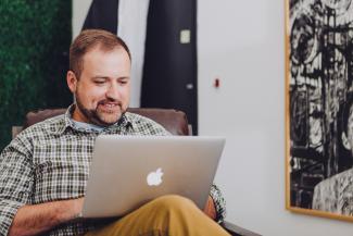 man smiling and using MacBook by Jud Mackrill courtesy of Unsplash.