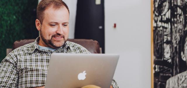 man smiling and using MacBook by Jud Mackrill courtesy of Unsplash.